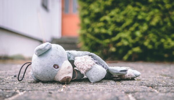 A worn, light-blue stuffed teddy bear lying abandoned on the ground outdoors, slightly dirty and weathered.